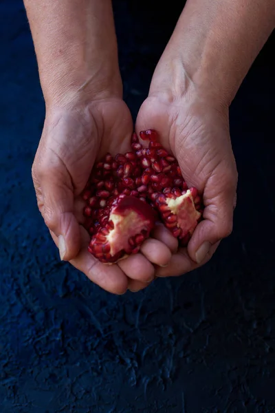 Kärnor av granatäpple i händerna på en man på en mörk bakgrund — Stockfoto