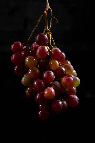 Um monte de uvas vermelhas em um fundo preto com gotas de orvalho — Fotografia de Stock