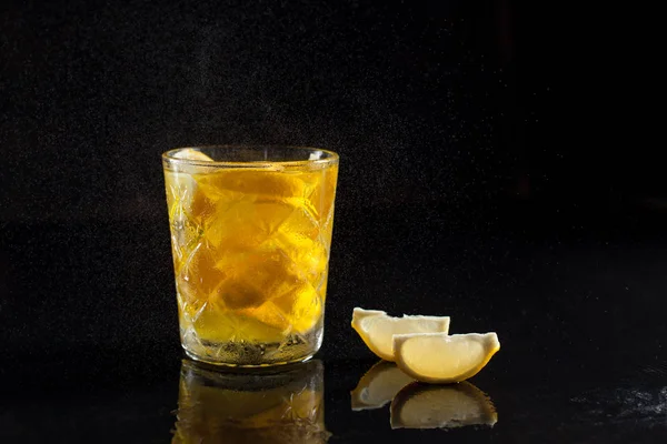 Cóctel de limón en un vaso sobre un fondo negro con rodajas de limón y gotas salpicaduras con reflexión sobre un fondo negro — Foto de Stock