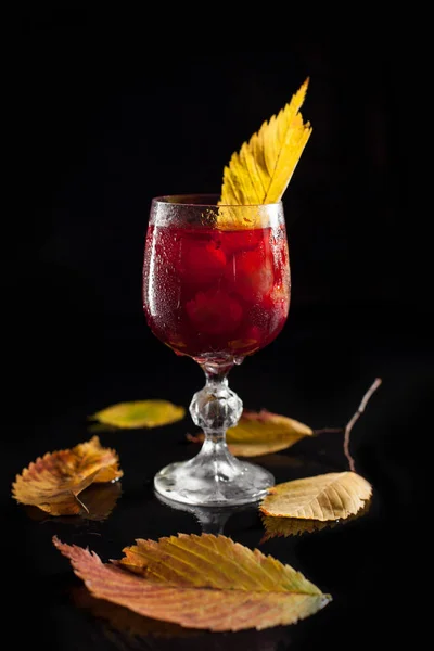 Un verre avec des raisins et du vin sur un fond de bois noir entouré de feuilles d'automne — Photo