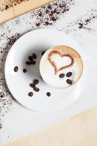 Xícara de café em um pires branco com grãos de café com tortas e bolos em uma placa de corte branca, em um fundo de madeira — Fotografia de Stock