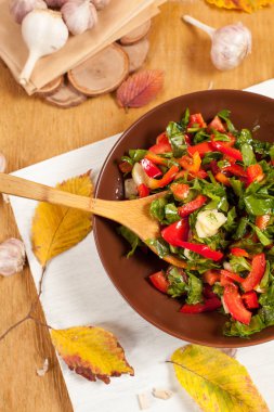tereyağı ve sarımsak sonbahar yaprakları tarafından çevrili bir ahşap zemin üzerine beyaz kesme tahtası üzerinde kahverengi bir tabakta sebze salatası