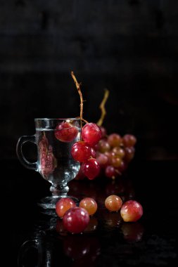 bir bardak üzüm çilek ve siyah bir zemin üzerine üzüm demet