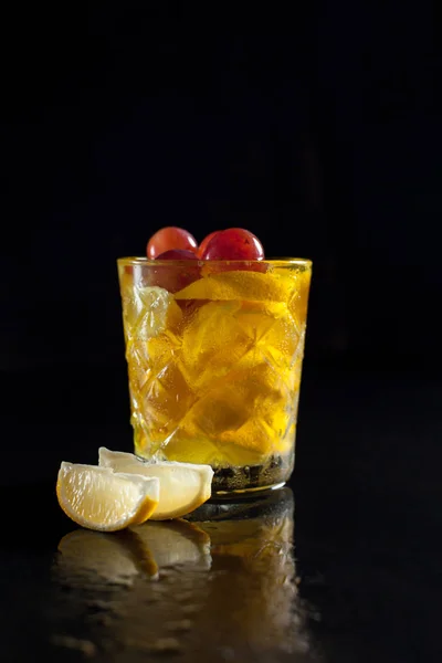 Cocktail di limone in un bicchiere su fondo nero con fette di limone e gocce spruzzate con riflessione su fondo nero — Foto Stock