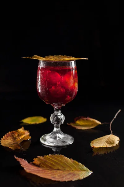 Un bicchiere con uva e vino su fondo di legno nero circondato da foglie autunnali — Foto Stock