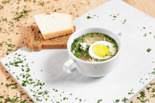 Sup kaldu daging dengan telur dan mie di piring putih di papan potong putih dengan sayuran hijau di latar belakang kayu — Stok Foto