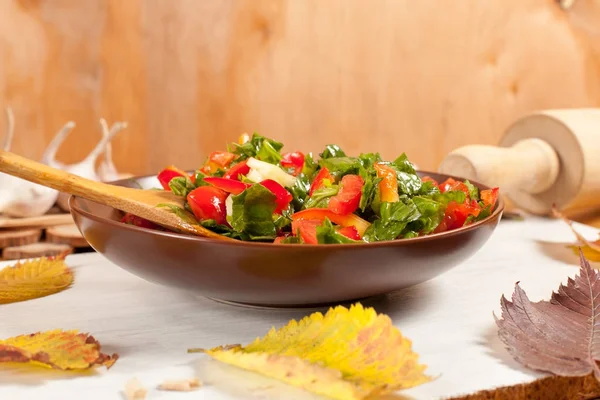 Ensalada de verduras con mantequilla y ajo en un plato marrón sobre una tabla de cortar blanca sobre un fondo de madera rodeado de hojas de otoño —  Fotos de Stock