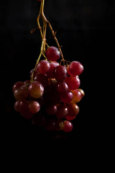 Um monte de uvas vermelhas em um fundo preto com gotas de orvalho — Fotografia de Stock