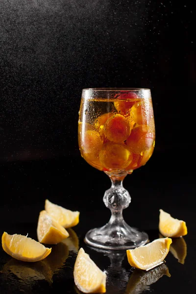 Un vaso con uvas, limón, vino y un racimo de uvas sobre un fondo negro con un goteo de gotas — Foto de Stock