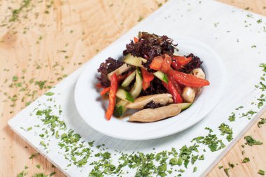 ahşap arka plan üzerinde beyaz bir tahta üzerinde beyaz bir tabakta yeşillikleri ile salatalık, biber, domates, lahana ve tavuk fileto ile sonbahar sebze salatası