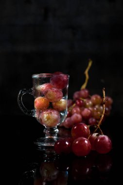 bir bardak üzüm çilek ve siyah bir zemin üzerine üzüm demet