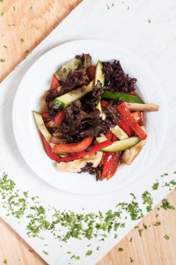 ahşap arka plan üzerinde beyaz bir tahta üzerinde beyaz bir tabakta yeşillikleri ile salatalık, biber, domates, lahana ve tavuk fileto ile sonbahar sebze salatası