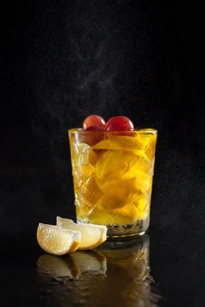 Cocktail van citroen in een glas op een zwarte achtergrond met plakjes citroen en spetterend druppels met reflectie op een zwarte achtergrond — Stockfoto