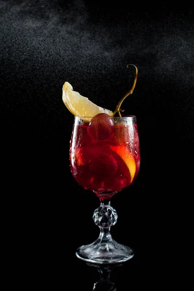 Een glas met druiven bessen, citroen, wijn en een tros druiven op een zwarte achtergrond met een dribbel van druppels — Stockfoto
