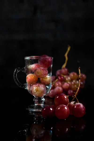 Бокал с ягодами винограда и гроздь винограда на черном фоне — стоковое фото