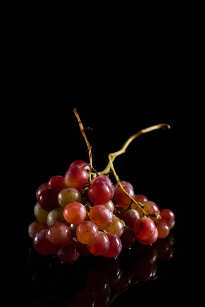 Um monte de uvas vermelhas em um fundo preto com gotas de orvalho — Fotografia de Stock