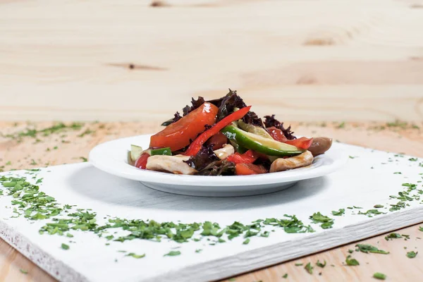 ahşap arka plan üzerinde beyaz bir tahta üzerinde beyaz bir tabakta yeşillikleri ile salatalık, biber, domates, lahana ve tavuk fileto ile sonbahar sebze salatası