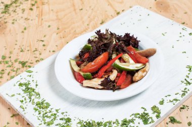 ahşap arka plan üzerinde beyaz bir tahta üzerinde beyaz bir tabakta yeşillikleri ile salatalık, biber, domates, lahana ve tavuk fileto ile sonbahar sebze salatası