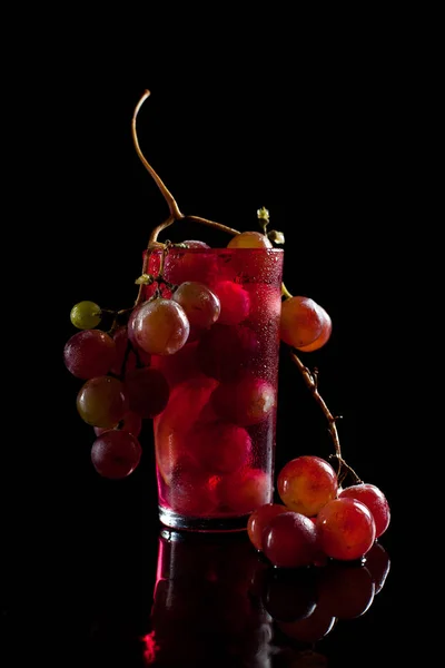 Un bicchiere con acini d'uva, vino e un grappolo d'uva su fondo nero con fusti di gocce — Foto Stock