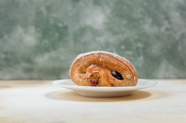 bir puf kek meyve doldurma ve çikolata beyaz tabakta ile pudra şekeri serpilir ve çikolata ile mavi bir arka plan üzerinde ahşap bir masaya döktü