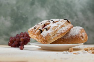 bir puf kek meyve doldurma ve çikolata beyaz tabakta ile pudra şekeri serpilir ve çikolata ile mavi bir arka plan üzerinde ahşap bir masaya döktü