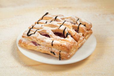 bir puf kek meyve doldurma ve çikolata beyaz tabakta ile pudra şekeri serpilir ve çikolata ile mavi bir arka plan üzerinde ahşap bir masaya döktü