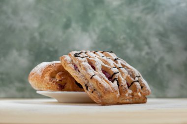 bir puf kek meyve doldurma ve çikolata beyaz tabakta ile pudra şekeri serpilir ve çikolata ile mavi bir arka plan üzerinde ahşap bir masaya döktü