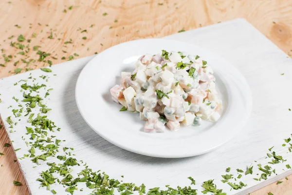 Olivier salata yeşillikleri ahşap arka plan üzerinde beyaz kesme tahtası üzerinde bir havlu üzerinde beyaz bir tabakta ile