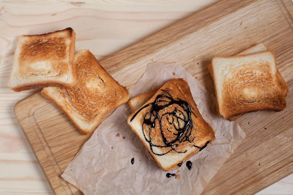 Çikolata ile ahşap kesme tahtası ahşap arka plan üzerinde kağıda döktü bir muz ile tost — Stok fotoğraf