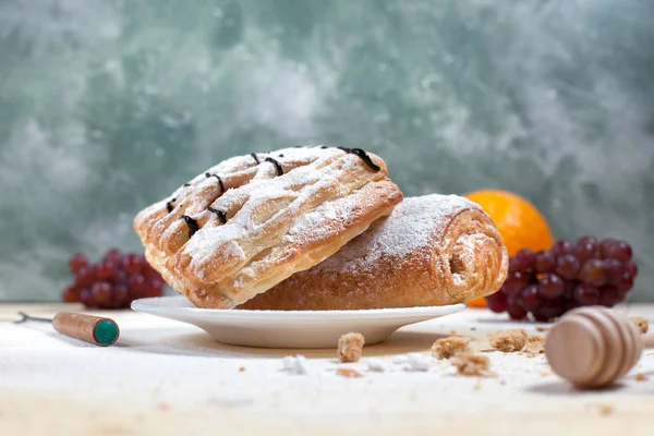 puf böreği berry doldurma ve çikolata, portakal ve üzüm ile ahşap arka plan üzerinde beyaz bir tepside pudra şekeri serpilir