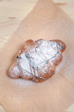 bir parça kağıt, ahşap bir zemin üzerine pudra şekeri serpilir çikolatalı kruvasan