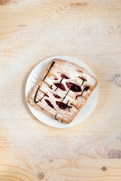 Puf böreği berry doldurma ve çikolata ile ahşap arka plan üzerinde beyaz bir tepside pudra şekeri serpilir — Stok fotoğraf
