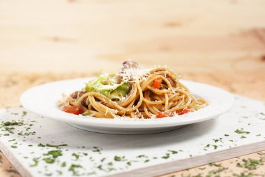 hafif ahşap arka plan üzerinde beyaz kesme tahtası üzerinde beyaz bir tabakta sebze ve et ile makarna otlar ile serpilir