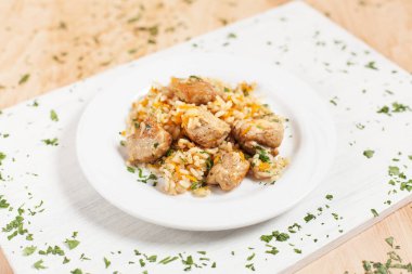 etli pilav ve sebze ışık ahşap arka plan üzerinde beyaz kesme tahtası üzerinde beyaz bir plaka üzerinde otlar ile serpilir