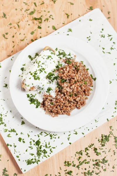 Grano saraceno con pesce sotto salsa su un piatto bianco su un tagliere bianco su uno sfondo di legno chiaro cosparso di erbe — Foto Stock