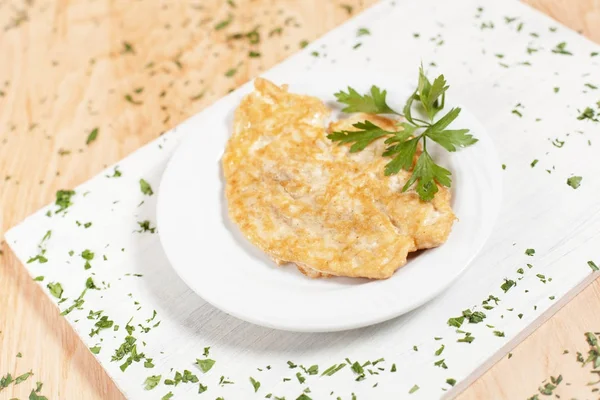 Chop cutlet in adonan on a white plate on a white cutting board on a light wood background sprinkled with herbs — Stok Foto