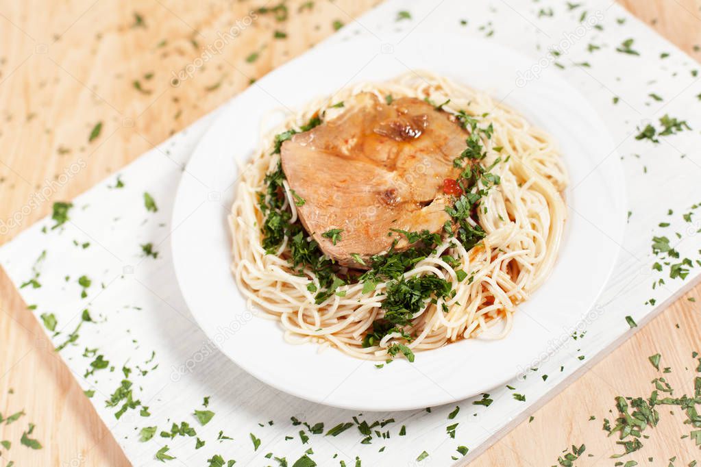 Spaghetti with steak on a white plate on a white cutting board on a light wooden background sprinkled with herbs