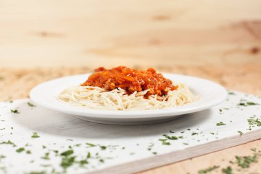Et ve otlar ile serpilir hafif ahşap arka plan üzerinde beyaz kesme tahtası üzerinde beyaz bir tabakta sos spagetti
