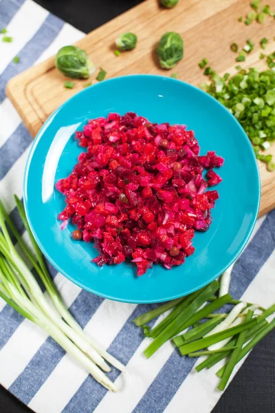 Salat mit Roter Bete, grüne Zwiebel auf einem Holzschneidebrett, gestreiftes Küchentuch auf dunklem Holzgrund — Stockfoto