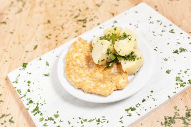 bir meyilli ahşap arka plan otlar ile serpilir ateşin üzerinde beyaz kesme tahtası üzerinde beyaz bir tabakta patates ile doğrayın