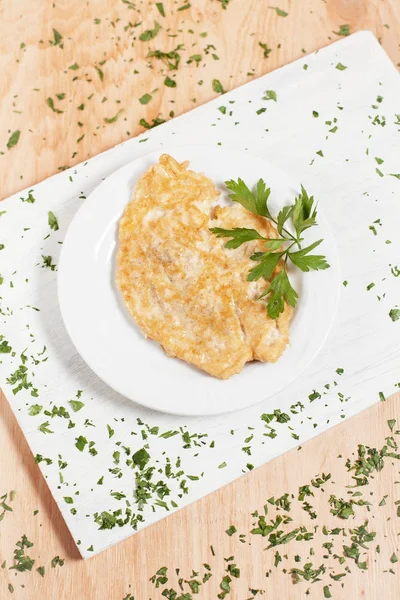 Chop cutlet in adonan on a white plate on a white cutting board on a light wood background sprinkled with herbs — Stok Foto