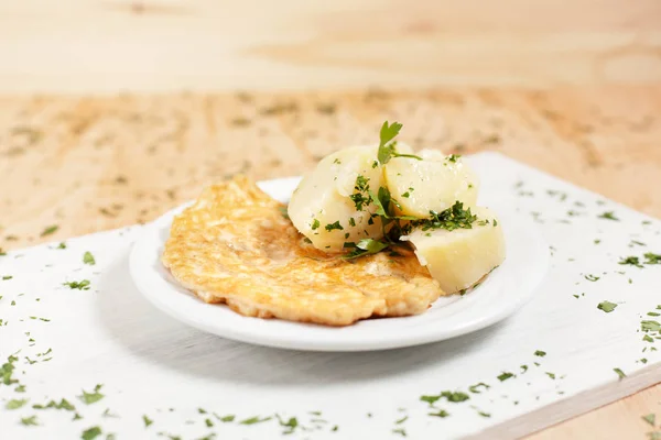 Memotong adonan dengan kentang di piring putih pada papan potong putih di atas kayu cahaya latar ditaburi dengan herbal — Stok Foto