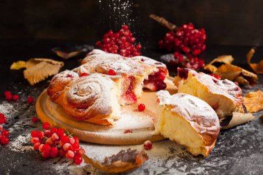 Bir yuvarlak ahşap tahta sürgünler ve sonbahar yaprakları çilek tarafından çevrili siyah ahşap zemin üzerinde pudra şekeri serpilir berry kek,