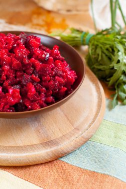 Geleneksel Rus pancar salatası salata yeşilliklerle çevrili bir çizgili havlu üzerinde ahşap kesme tahtası üzerinde bir kahverengi kil kase