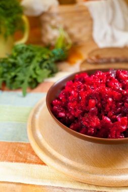 Geleneksel Rus pancar salatası salata yeşilliklerle çevrili bir çizgili havlu üzerinde ahşap kesme tahtası üzerinde bir kahverengi kil kase