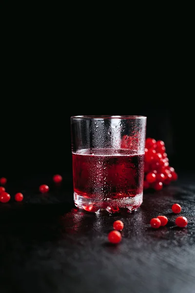 Um copo de nevoeiro com um coquetel vermelho e uma rosa guelder em um fundo preto e molhado — Fotografia de Stock