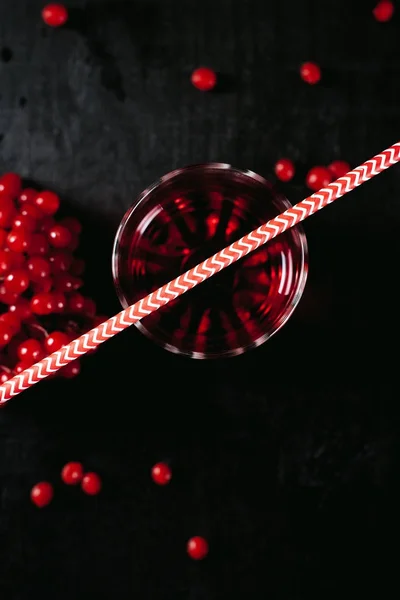 Ett dimmigt glas med en röd cocktail och en guelder rose på en svart, våta bakgrund — Stockfoto