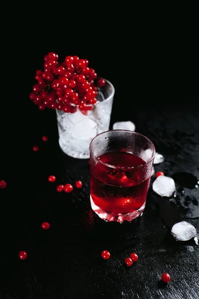 Due bicchieri congelati con un cocktail rosso e ghiaccio, con un guelder rosa su uno sfondo nero bagnato e spruzzi — Foto Stock