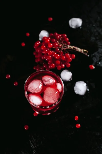 A foggy glass with a red cocktail of ice and guelder rose on a black, wet background — Stock Photo, Image