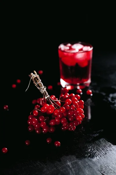 Un bicchiere nebbioso con un cocktail rosso di ghiaccio e guelder rosa su uno sfondo nero e bagnato — Foto Stock